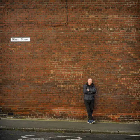 Simon Hill HonFRPS Former miner standing against a brick wall