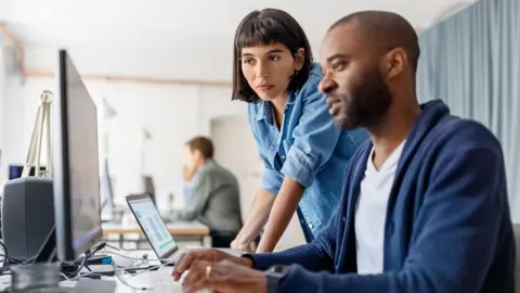 A man and a woman looking at a computer screen in an office