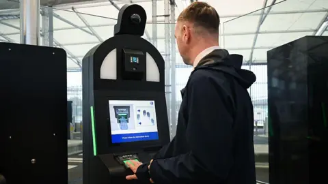 Getty Images A man in a black coat putting his fingers on a biometric machine to have his fingerprints taken.