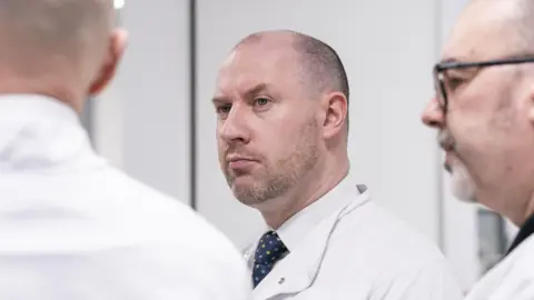 NHS Scotland staff vote to accept two-year 8% pay offer 6 PA Media Neil Gray who is wearing a white lab coat over a shirt and tie, is standing between tow other men