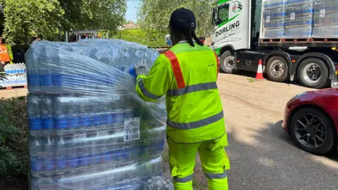 BBC A worker in hi-vis opens a pallet of water bottles beside an HGV.