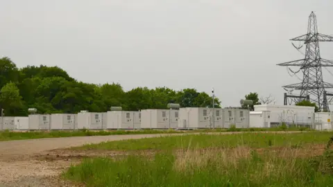 A rural site containing rows of large metal boxes that resemble shipping containers.