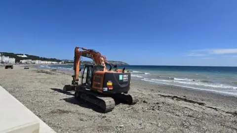 A large excavator smooths out a layer of sand on the beach