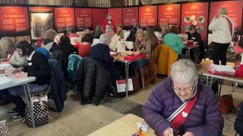 Pat Kellett Women seated in York Minster sewing sanitary kits