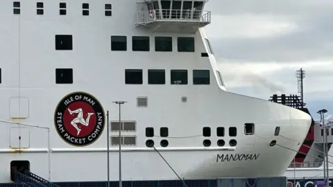 BBC A close up of the bow of Manxman, it is a large boxy white ferry, with a logo reading Isle of Man Steam Packet and the three legs of man.