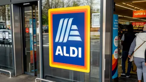 The front entrance to a branch can be seen with the shop's logo on a glass door and shoppers inside.