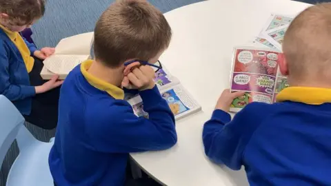 Two boys and a girl sat at a table reading books. 