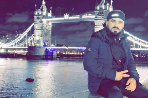 NCA Man at night wearing all black posing outside tower bridge in London