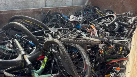 A skip is filled with dozens of bikes, with their frames and wheels all tangled together. 
