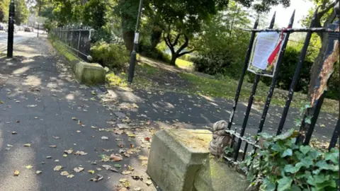 One of the entrances to Leazes Park with railings on either side. Two concrete bases are on either side of the entrance but are missing the pillars.