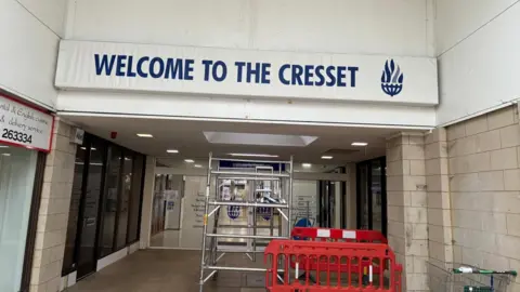 Shariqua Ahmed / BBC The entrance to the Cresset - a white board with blue writing - and some metal scaffolding in front of it.