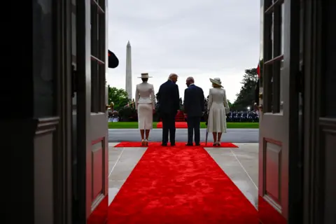 AFP via Getty Images The backs of the two couples are silhouetted against the backdrop of the Washington monument through the doors of the White House.
