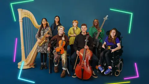 A group of musicians pose together with their instruments. They are in front of a deep blue backdrop, with neon lines framing the edges of the image in green, pink, blue and yellow. There is a large pale wooden harp on the left, next to a female musician holding a saxophone, there are two musicians sat down at the front, one holding a violin and one a cello. Behind them is a women holding a clarinet and another holding an electric bass guitar and to the right is a woman in a wheelchair holding an iPad.
