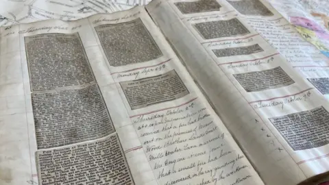 Leeds Museums An open historical scrapbook laid flat across a surface, with its pages spread wide. Each page is neatly ruled into sections, with printed newspaper cuttings pasted into columns.