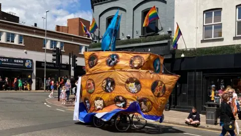 A group of cyclists with a large depiction of Noah's ark covering them