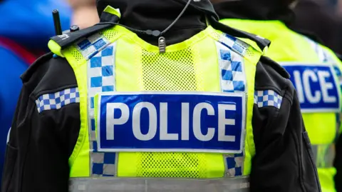 Police officer wearing a yellow vest with police wrote on the back.