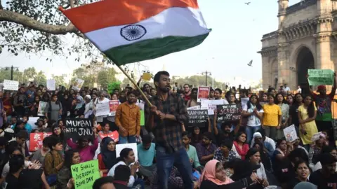 Getty Images Protesters and students shout slogans and hold Indian flags as they protest against the violent clashes
