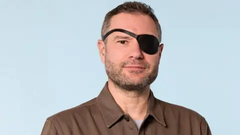 Headway David Baker wearing a brown shirt and a black eye patch over his left eye