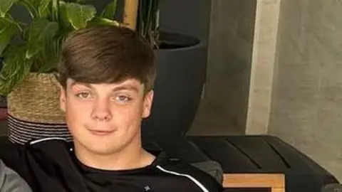 Family handout Harry smiles at the camera, he wears a black t-shirt and has short brown hair with a side-swept fringe