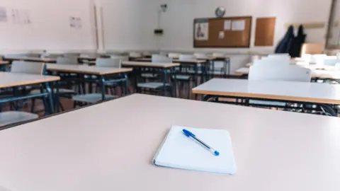 Getty Images An empty classroom with a notebook and pen on a table.