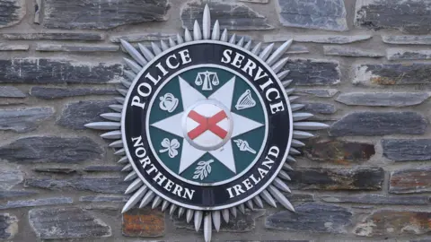 Police service of Northern Ireland badge on brick wall.