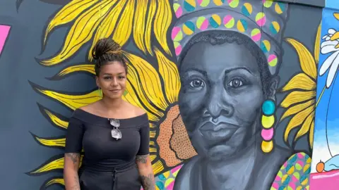 Johnnie Wright/BBC Lily Hammond in front of her mural at Ipswich waterfront of Maya Angelou