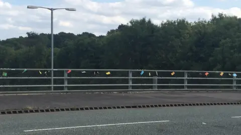 A series of small, colourful notes attached to a bridge over the A14 in Northamptonshire.