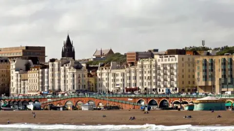 Getty Images A picture of Brighton beach and pier; walkways down to the pier are visible, as is the sand. A number of apartment buildings are also visible below the skyline.