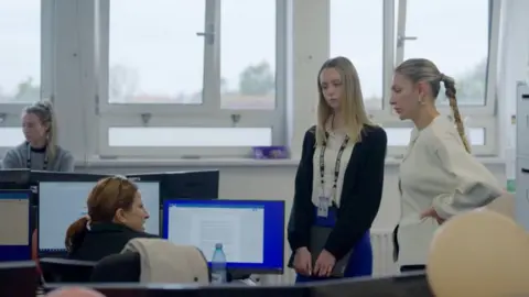 Two ladies speak to a third working at her computer