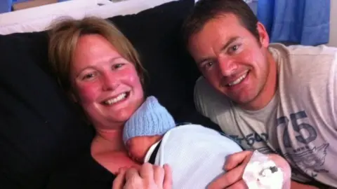 Gill castle Gill holds a baby with her husband smiling next to her