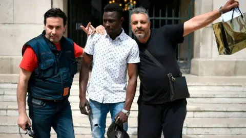 Getty Images A 22-year old Mamoudou Gassama from Mali (C) poses with passers-by in front of the town hall of Montreuil, an eastern Paris suburb, on May 28, 2018