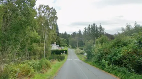 Picture of the B862 road through Whitebridge, with trees and greenery on either side and a small house to the left.