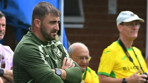 Richard S Brown Andy Cook in a green Canaries coach top watches a match from the sidelines