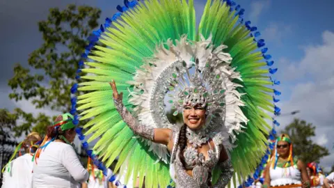 PA a woman at carnival wearing silver costume with green and blue feathesr