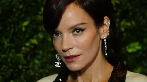 PA Media Lily Allen, digambarkan dengan rambut hitam model up dengan poni samping, eye liner bersayap, dan beberapa anting berlian