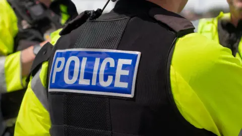 Back of police officer who is wearing high vis jacket and black coat with words 'police' in white.