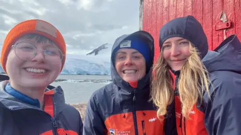 Aoife McKenna Three woman smiling while stood outside in Port Lockroy, Antarctica
