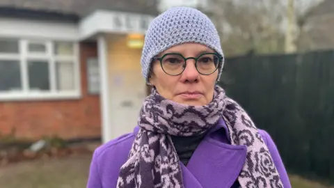 Ursula Bilson looking at the camera wearing a purple hat, scarf and coat.