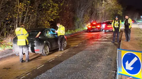 Four Surrey Police officers pulling drivers over during Operation Limit. Three cars, two black and one red, can be seen in the image. All four officers are wearing high-viz jackets.