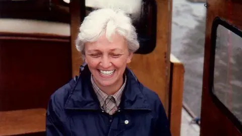 Family photo Shelia Hartman is pictured smiling on a boat. She has white hair and wears a navy blue anorak. 