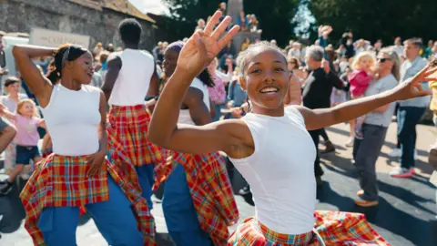 Adrienne Photography A group of young dancers perform in the street watched by a crowd of people.