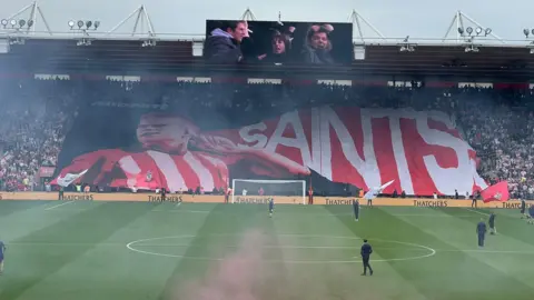 A Saints banner being held in the crowd by fans, visible across the pitch