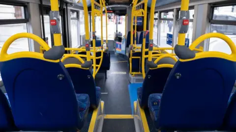 A view from inside an empty bus, looking towards the driver's compartment. The seats are blue, with yellow metal trim. 