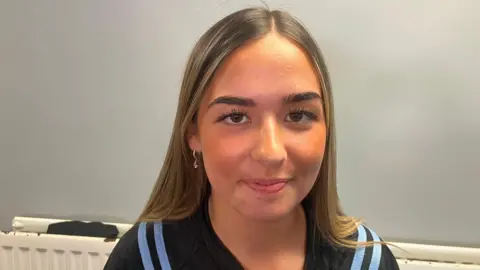 Cora Nelis has long fair hair and is wearing a navy and light blue sports top 
