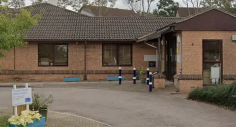 Google A single-storey office building with a brown roof. A sign at the front reads "Thomas Edward Mitton House".