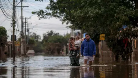 Getty Images People walk through a flooded street in the Chacara neighborhood in Eldorado do Sul, Rio Grande do Sul state, Brazil, on May 22, 2024.