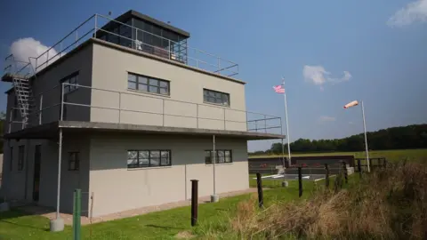 Shaun Whitmore/BBC A large three-storey grey control tower with balconies in a field.