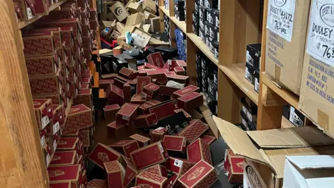 Todd Dunaway Shoe boxes strewn on the floor between two shelves in a sportswear store.