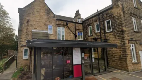 An older stone built building with several windows has a modern glass single storey extension on the front