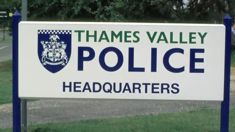 Thames Valley Police Headquarters sign - written in green and blue writing on a white background, photo has greenery in the background.